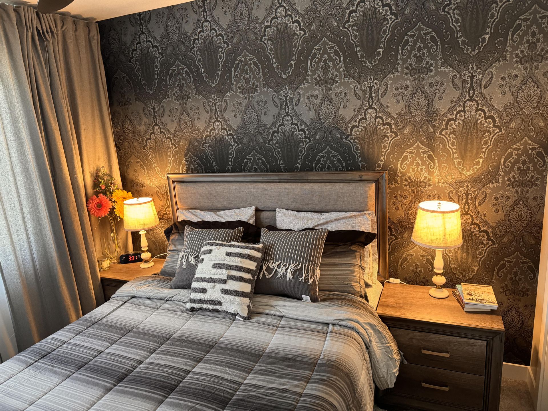 The Queen HomeStay Suite — a neatly made bed against patterned wallpaper